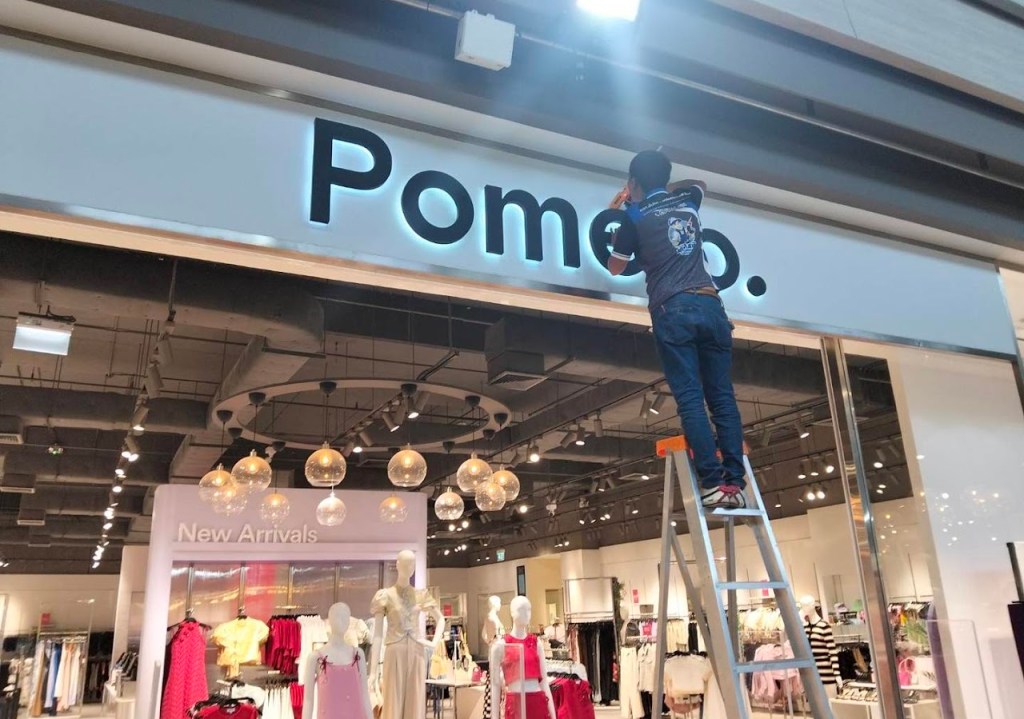 คนงานกำลังติดตั้งป้ายชื่อร้าน Pomelo ที่หน้าร้านในห้างสรรพสินค้า